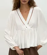 Blusa femenina tipo bata de viscosa color blanco, con escote en V cruzado y detalle calado. Presenta mangas largas con puños ajustados, corte amplio con recorte fruncido bajo el busto y diseño fluido.