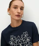 Remera de algodón color azul marino, con cuello redondo, mangas cortas y un bordado frontal en color blanco con diseño simétrico de motivos florales.