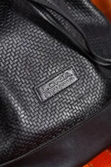 Cartera tipo botellero color marrón con efecto trenzado, tamaño mediano, cierre con frunce, correa ajustable con hebilla para usar al hombro o cruzada, doble bolsillo interior (uno con cierre).