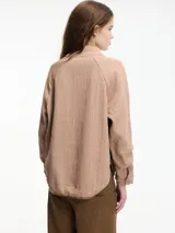 Sobrecamisa color beige, confeccionada en algodón texturizado (tipo guateado o nido de abeja), con cuello alto abotonado y mangas raglán.