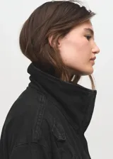 Anorak de estilo utilitario confeccionado en tejido de algodón tipo denim, con diseño oversize, cuello embudo, cierre frontal de cremallera y botones a presión, y cuatro bolsillos de parche con solapa en la parte delantera.