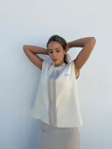 Top sin mangas tejido en hilo color crema, con cuello redondo y rayas verticales grises. Presenta un logo bordado en el pecho.