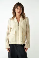 Campera de lana fina color crema, con cierre frontal y cuello tipo solapa. El cuerpo es de tejido acanalado y las mangas son de tejido de punto calado.