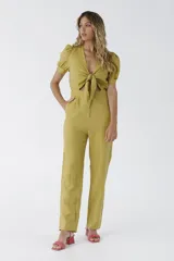 Mono de mujer color verde mostaza, con escote en V y nudo frontal que deja ver un corte en la cintura. Presenta mangas cortas abullonadas y pantalón de corte recto.