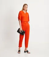 Pantalón zanahoria color naranja, marca Cortelle, con pliegues, bolsillos laterales y traseros, detalle de botón en los bajos y cierre en la cintura por botón.