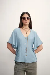 Camisa celeste con cuello en V, mangas cortas con volados, cierre frontal con botones y lazos ajustables en los laterales.