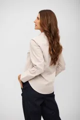 Camisa de corte clásico con cuello camisero, cierre frontal de botones y bolsillo en el pecho. Presenta un diseño de rayas verticales finas en tonos beige y blanco.