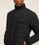 Campera puffer negra con cuello alto, cierre frontal con botones a presión, bolsillos laterales y un bolsillo cargo en el pecho. Presenta un diseño acolchado y forro interior suave.