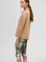 Camisa sin mangas tipo musculosa confeccionada en denim liviano de color tostado. Presenta cuello camisero y cierre frontal con botones. Destaca por sus bordados coloridos en el pecho con motivos veraniegos como sol, olas y elementos marinos.