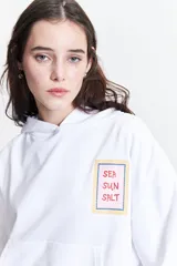 Canguro blanco de felpa con capucha ajustable, bolsillos frontales tipo canguro y estampado en frente y espalda.