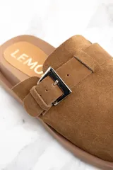 Zueco de cuero color marrón claro, con hebilla metálica plateada ajustable y suela plana con ranuras.