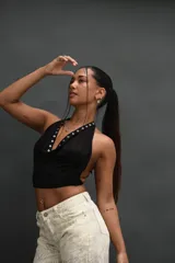Top negro tipo halter, ajustado al cuerpo, con escote drapeado y detalles de ojales metálicos plateados a lo largo del borde del escote.