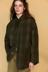 Chaqueta de algodón encerado con diseño de cuadros en tonos verde oliva, beige y líneas rojas. Presenta cuello solapa, cierre frontal con botones a presión metálicos, bolsillos de plastrón con solapa y un detalle de pañuelo desmontable sobre los hombros.