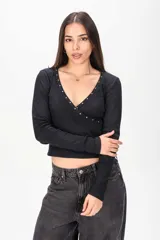 Remera manga larga blanca de tejido acanalado, con profundo escote en V cruzado decorado con tachas metálicas en los bordes.