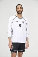 Camiseta de fútbol blanca con cuello en V y mangas largas con puños a rayas negras. Tiene un logo de la marca en el pecho y el número 92 en el centro.