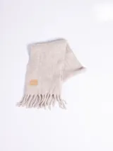 Bufanda de tejido grueso en color gris oscuro, con flecos en los extremos y etiqueta de cuero sintético con el logo de la marca en una de las puntas.