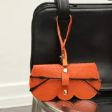 Estuche para lentes de ecocuero color naranja con textura granulada, diseño de solapa con botones a presión metálicos y correa de mano integrada.