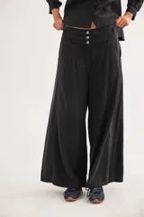 Pantalón de jean con diseño de tiro medio-bajo y piernas anchas. Presenta una pretina ancha con cierre de tres botones metálicos frontales, pinzas decorativas en la cintura y bolsillos delanteros funcionales.