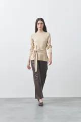 Polera de tejido de punto color beige, con cuello alto, manga larga y detalle de lazo ajustable en la cintura que aporta estructura a la silueta.