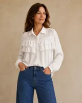 Camisa blanca de manga larga con cuello camisero, cierre frontal de botones y detalles de volados con bordado broderie en el frente.