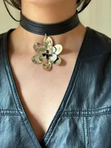 Gargantilla tipo choker de cuero sintético negro con dije de flor plateada y centro con cuentas negras.