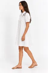 Vestido camisero midi de lino natural color blanco, con silueta fluida de línea A, cuello camisero, mangas cortas y un elaborado bordado de pedrería y cristales con diseño de estrellas en el hombro.
