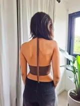 Crop top marrón de escote profundo en V con diseño tipo halter que incluye una banda integrada al cuello. Presenta un ajuste entallado con detalle de frunces en la parte inferior.