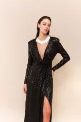 Vestido largo de lentejuelas color negro, con escote profundo en V, mangas largas y tajo lateral en la falda. Presenta un diseño cruzado con fruncido en la cintura y espalda elastizada.