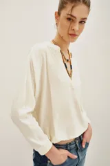 Remera de algodón color crudo, con cuello en V y mangas largas. Presenta un diseño holgado con puños tejidos y detalle de costura central en el escote.