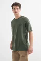 Remera de algodón color verde oliva, con cuello redondo y mangas cortas tipo ranglán. Presenta un pequeño estampado tonal en el pecho.