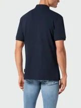Polo de piqué azul marino con cuello clásico, tapeta de botones y logo metálico en el pecho.
