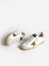 Zapatillas Golden Goose modelo Super-Star, de cuero blanco con estrella de cuero color cuero, refuerzo del talón con purpurina rosa, lengüeta de ante gris hielo y cordones color crema.
