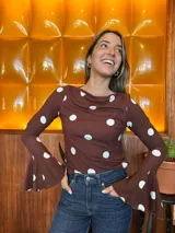 Blusa de manga larga ajustada al cuerpo, color marrón con estampado de lunares blancos. Presenta un cuello redondo con caída suave y mangas acampanadas con volados en los puños.