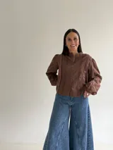 Blusa de brodery color blanco, con cuello redondo, mangas largas abullonadas con puños elásticos y cierre frontal con botones forrados. Presenta detalles de puntillas verticales en el frente.