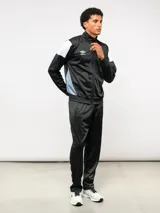 Conjunto deportivo Umbro compuesto por campera de cuello alto con cierre frontal y pantalón de corte recto. La campera presenta bloques de color blanco en los hombros y el logo de la marca bordado en el pecho. Confeccionado en tejido sintético con acabado satinado.