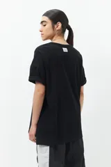 Remera blanca de algodón, corte oversized y manga corta, con cuello redondo y detalle de tres botones metálicos en cada lateral inferior.