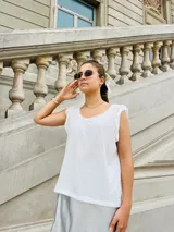 Blusa blanca sin mangas con cuello redondo y detalle de volados en los hombros.