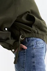 Campera verde militar sin cuello, con elástico y cinto regulable en la cintura, bolsillos amplios y cierre frontal.