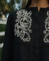 Camisa marrón chocolate de manga larga con bordado artesanal floral en hilo crudo sobre el pecho. Cuenta con cuello con sutil volado, cierre frontal de botones y mangas abullonadas con puños ajustables.
