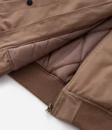 Campera bomber de sarga color tostado con cuello desmontable de pelo sintético oscuro. Presenta cierre frontal de cremallera, puños y cintura acanalados, y bolsillos laterales.