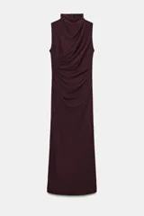 Vestido midi de color negro, con cuello subido y diseño sin mangas. Presenta un detalle de drapeado lateral en la parte delantera y cierre de cremallera oculta en la espalda.