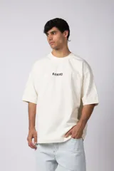 Remera oversize de color blanco hueso, con cuello redondo y manga corta ancha. Presenta un pequeño bordado frontal con la palabra "REWIИD" en negro.