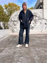 Campera tipo hoodie confeccionada en tejido de textura tipo corderito negro, con diseño de collage en la espalda que incorpora parches en gris, blanco y un cuadrado rojo, además de detalles de líneas verticales blancas. Presenta capucha y corte holgado.