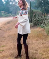 Vestido midi de punto color marfil, confeccionado artesanalmente en lana merino, con silueta en A, mangas largas oxford y cuello a la base. Presenta un diseño de bloques de color con bordados hechos a mano con motivos paisley y florales en tonos marrones, azules y rosados en la parte superior y las mangas.