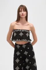 Top cropped negro, estilo strapless, con elástico en el busto y ruedo, y bordados blancos con motivos florales y geométricos.