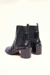 Bota tipo botineta de cuero negro con diseño trenzado artesanal en toda la capellada. Presenta paneles laterales elásticos, taco cuadrado de altura media y tirador en la parte superior trasera.