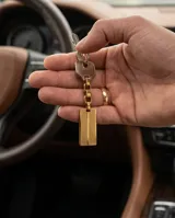 Llavero de acero con baño en oro, compuesto por un aro, una cadena de eslabones y una placa rectangular con textura grabada.