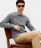 Suéter de punto de algodón con textura perlada, color gris melange. Presenta cuello polo con cierre de tres botones, manga larga y terminaciones acanaladas en puños y ruedo.