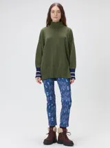 Pullover de punto color rojo, con cuello tortuga, corte holgado y mangas largas con puños acanalados en contraste con rayas blancas. Presenta un logo bordado en el pecho.