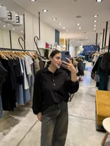 Blusa negra de manga larga abullonada con puños elásticos, cuello camisero y cierre frontal parcial de botones metálicos dorados.